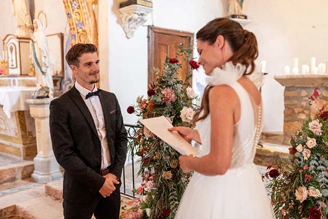 Une jeune mariée et son mari se tiennent face l'un l'autre dans un décor romantique d'église, partageant un moment