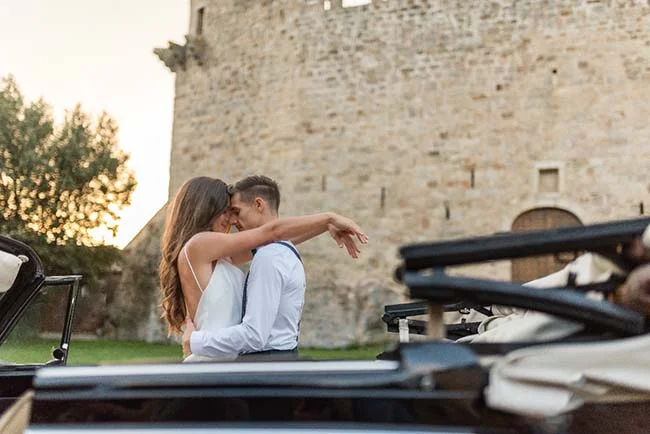 Un couple heureux dans une voiture convertible devant un château romantique.