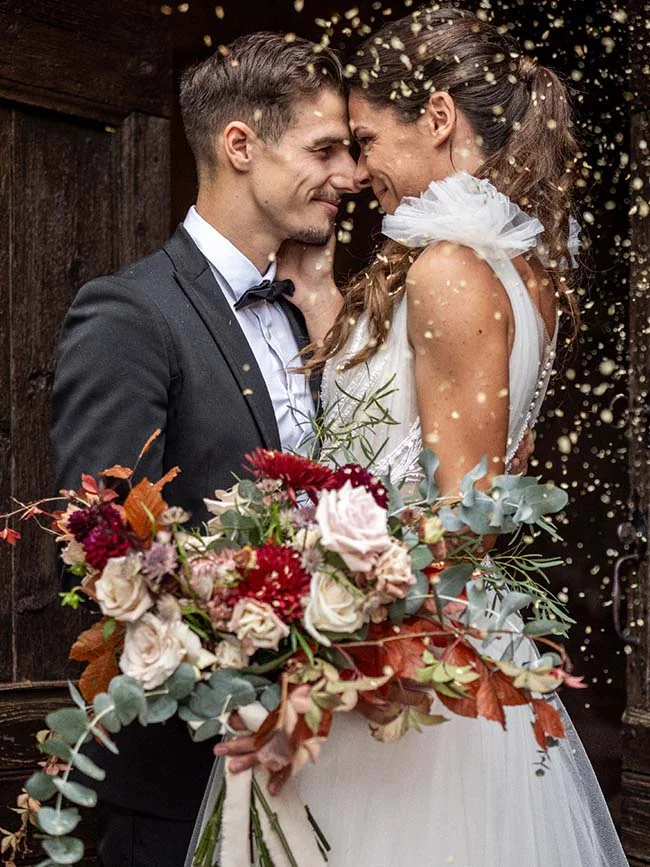 Un couple heureux se penche l'un envers l'autre, entouré d'un bouquet romantique et de confetti volant.