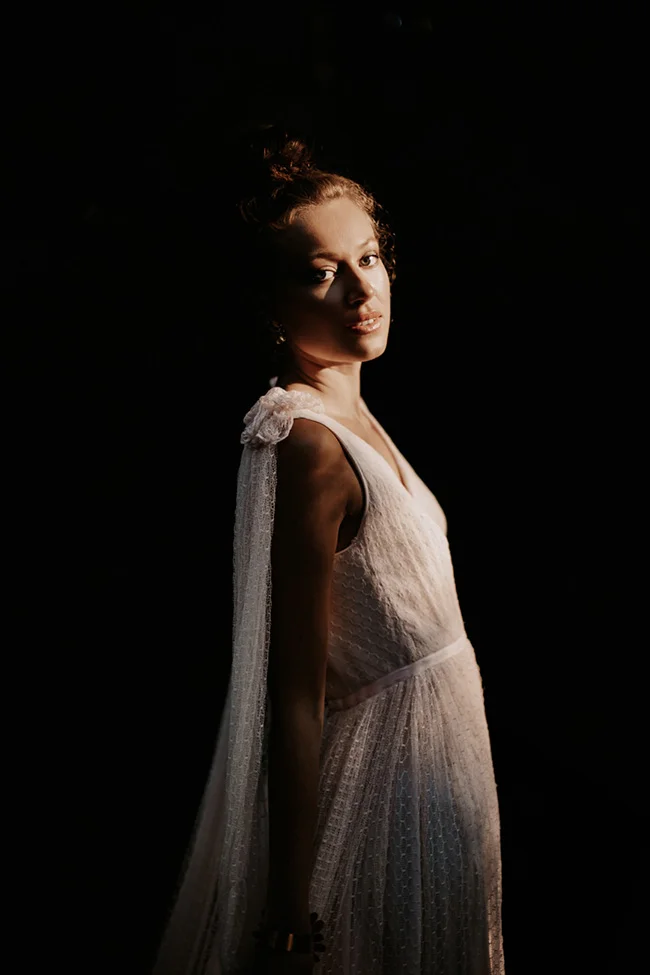 Portrait dramatique d'une mariée en robe blanche vaporeuse, éclairée en clair-obscur sur fond noir.