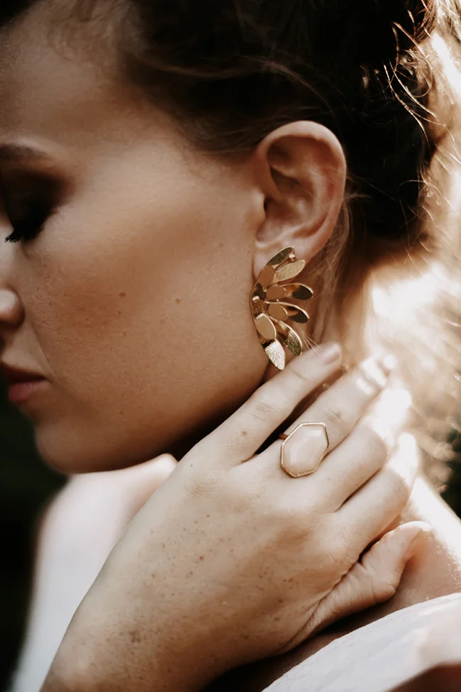Gros plan d'une mariée glamour portant des bijoux dorés, baignée d'une lumière chaude et naturelle.