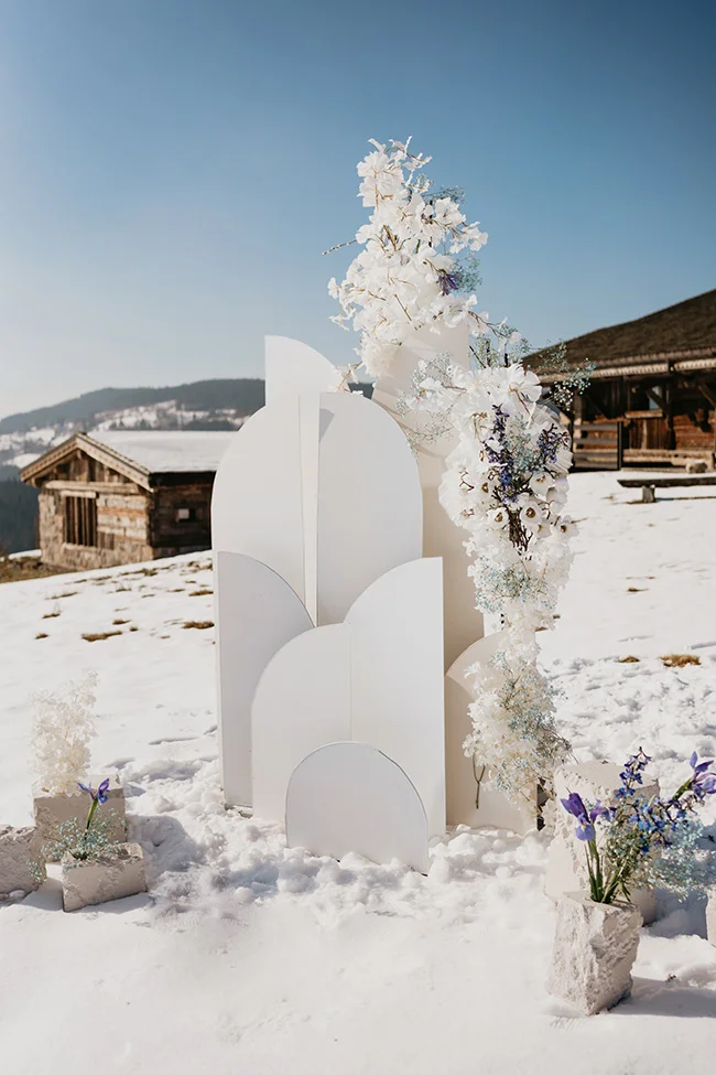 Décoration de cérémonie minimaliste blanche avec fleurs givrées dans un paysage de montagne enneigé.