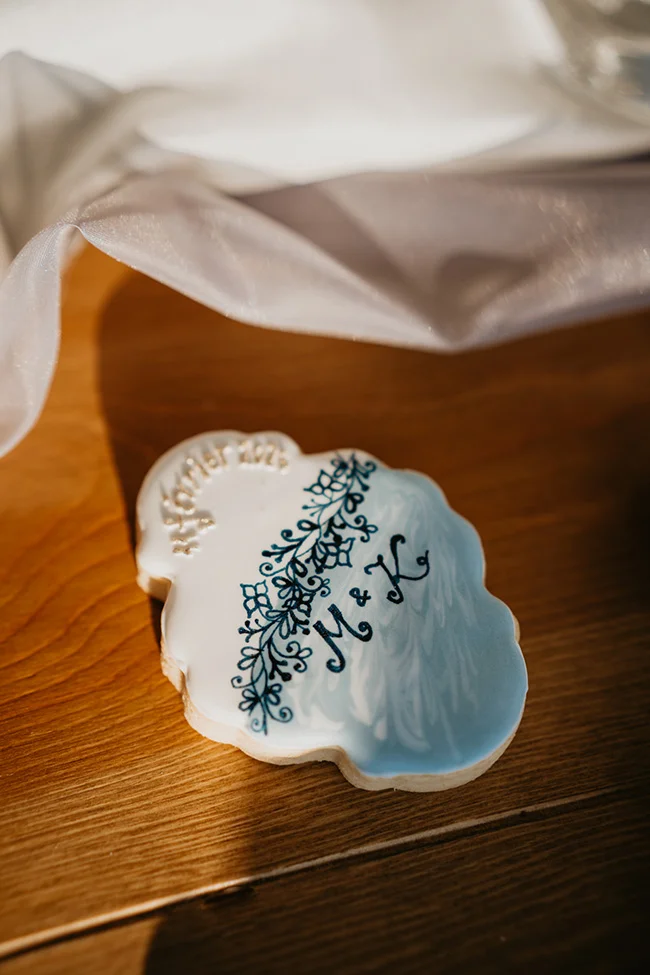 Biscuit personnalisé blanc et bleu avec initiales et motifs floraux, posé sur une table en bois aux tons chauds.