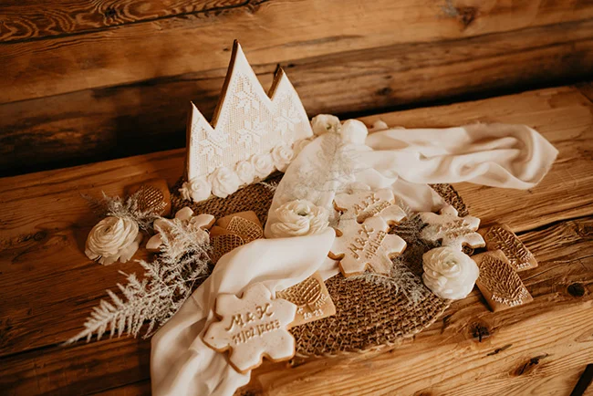 Biscuits personnalisés et décorations blanches sur un plateau en bois, ambiance hivernale et élégante.