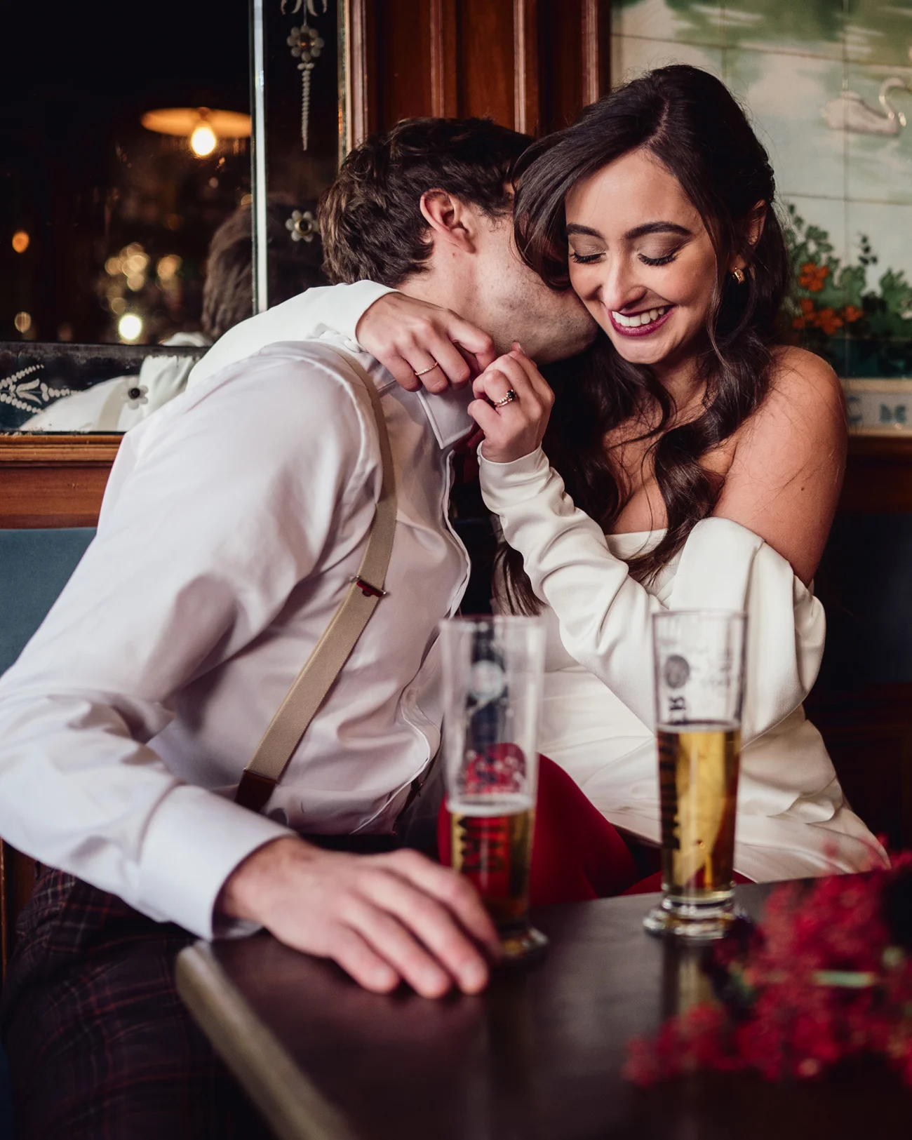 Couple complice en tenue rétro chic partageant un moment tendre avec des bières dans un pub chaleureux.