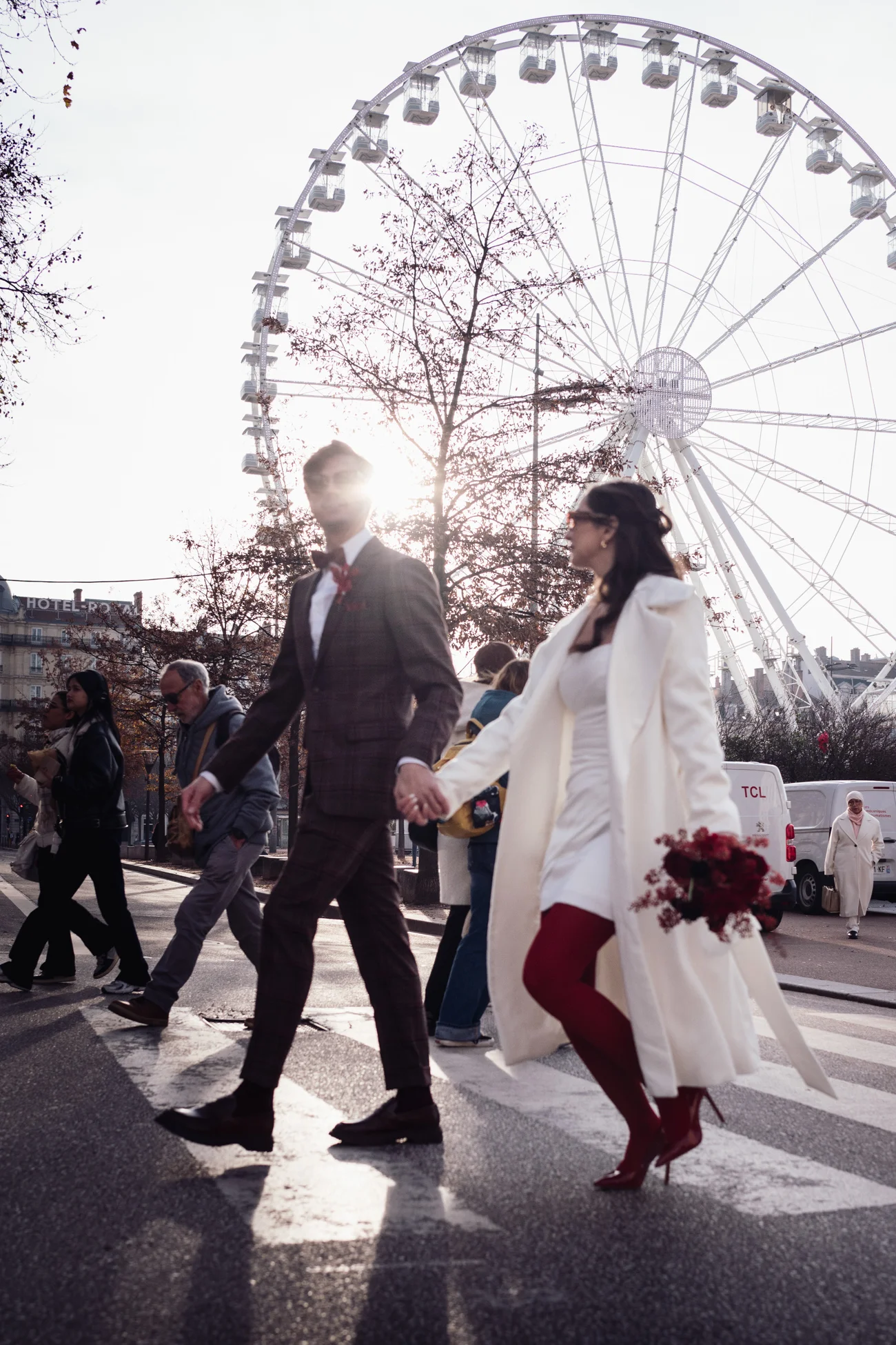 Couple rétro chic main dans la main traversant une rue à Paris devant une grande roue sous une lumière hivernale.