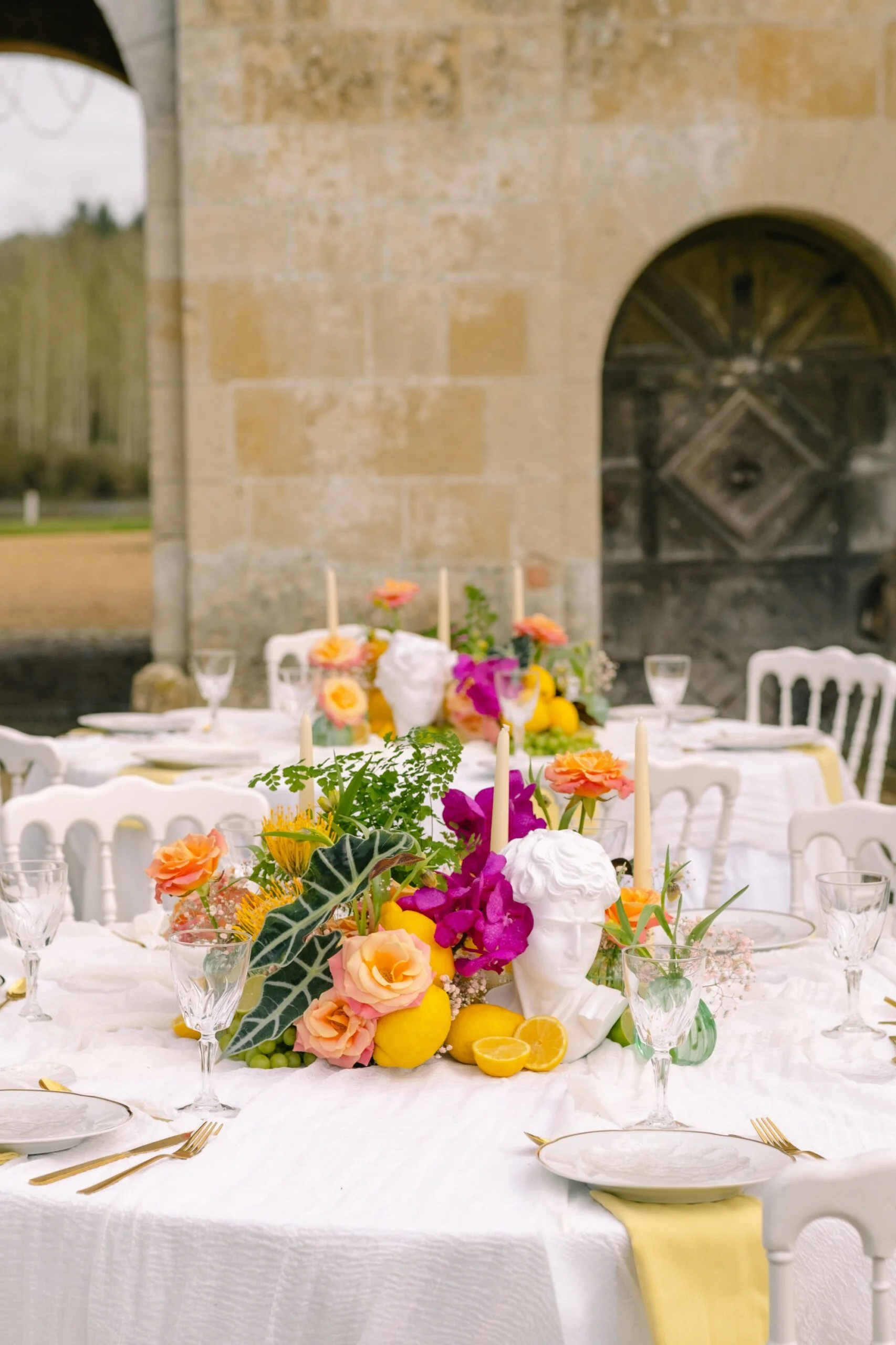 Table de mariage élégante avec centre de table composé de fleurs colorées, de citrons et d'un buste blanc classique.