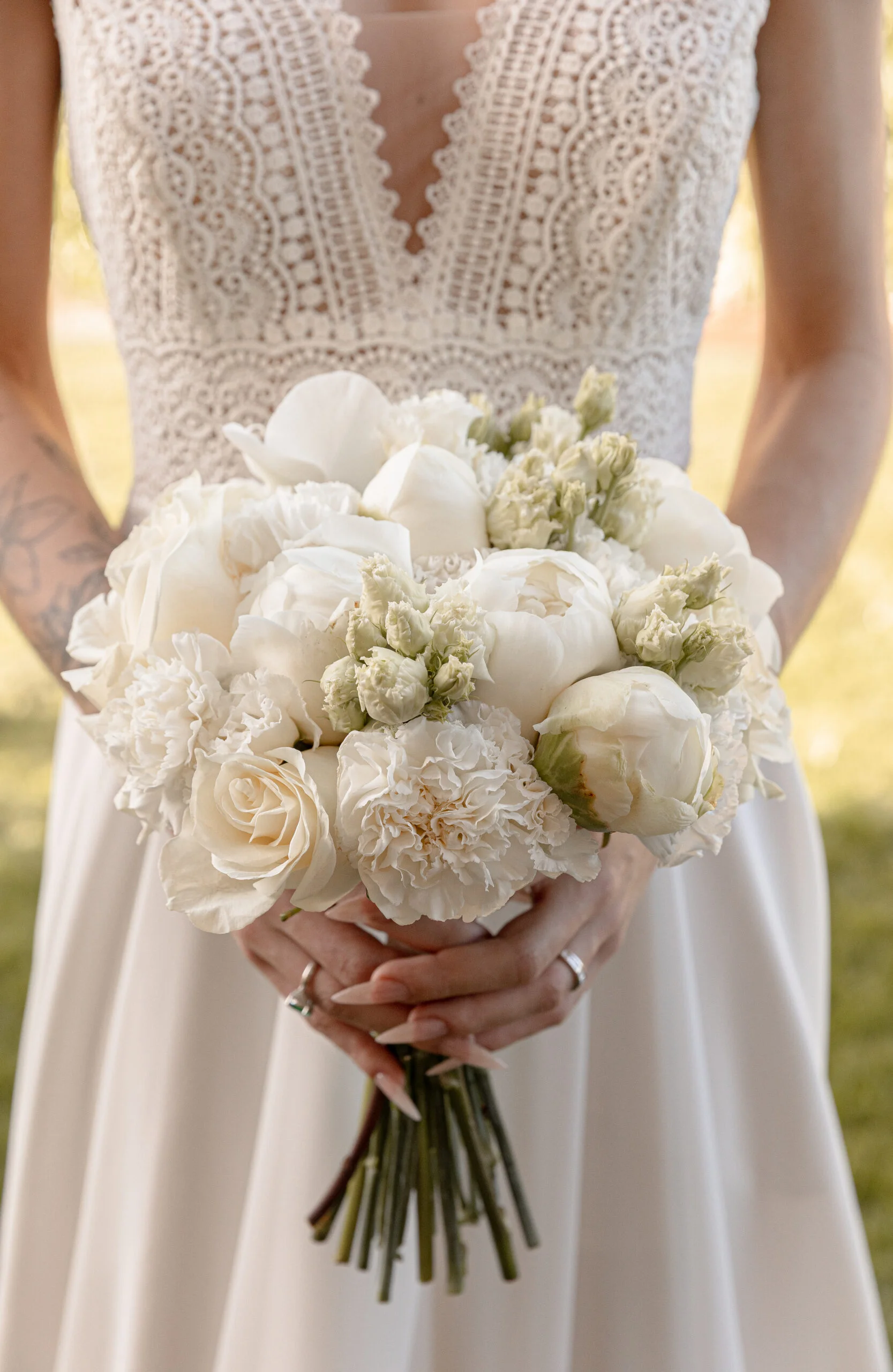 Mariée en robe de dentelle blanche tenant un bouquet de pivoines et roses blanches dans un style élégant et lumineux.