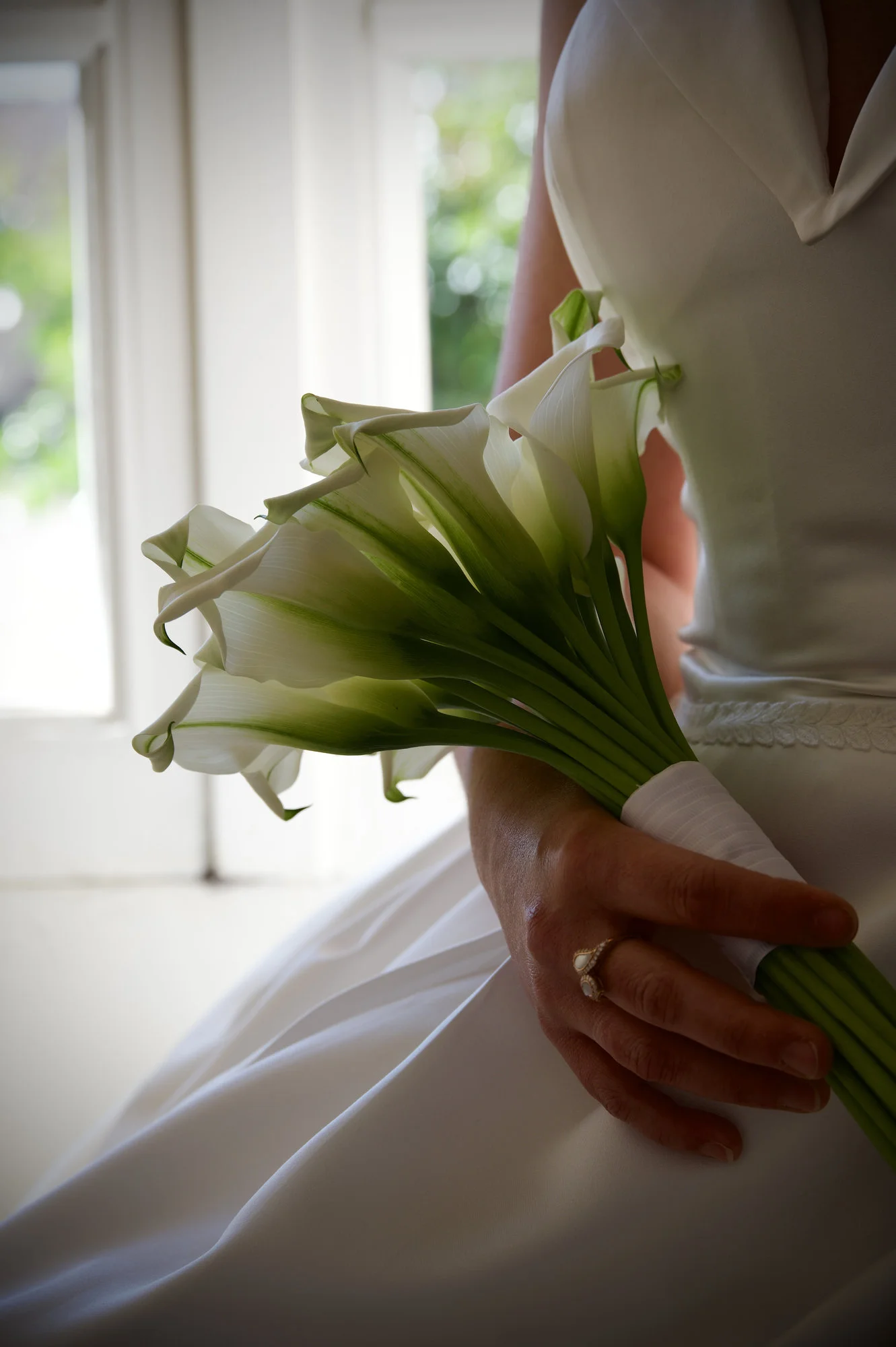 Mariée en robe blanche tenant un bouquet de callas blancs, ambiance lumineuse et élégante.