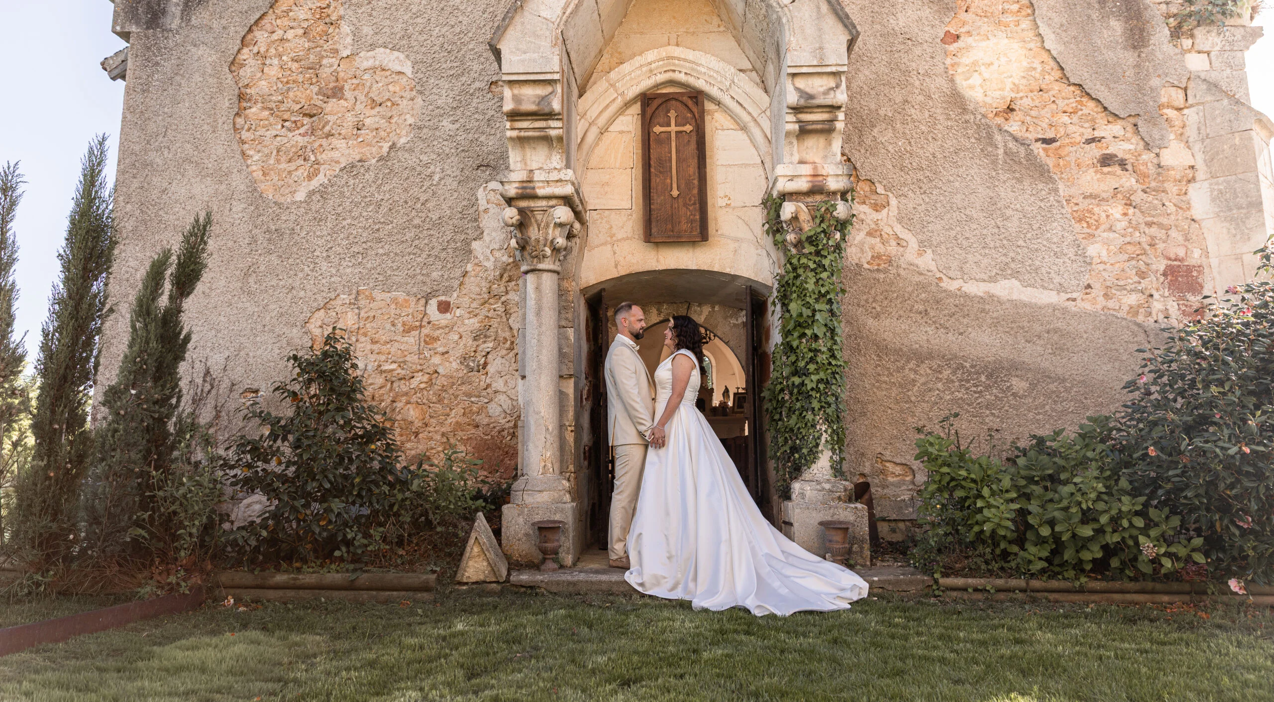 Couple de mariés s'embrassant devant l'entrée rustique en pierre d'un château dans une ambiance romantique et intemporelle.