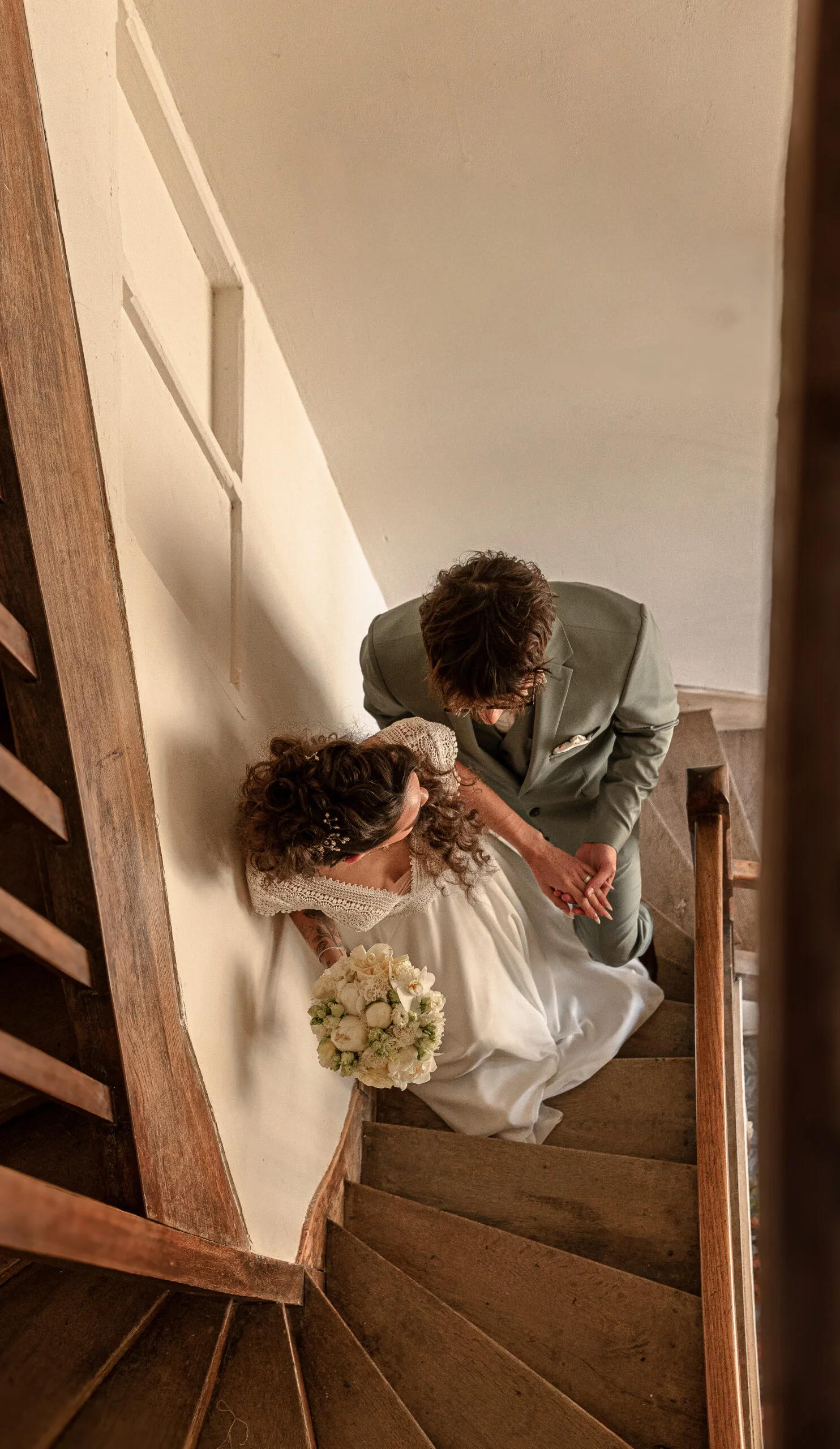 Vue plongeante d'un couple marié descendant un escalier en bois, ambiance romantique et élégante.