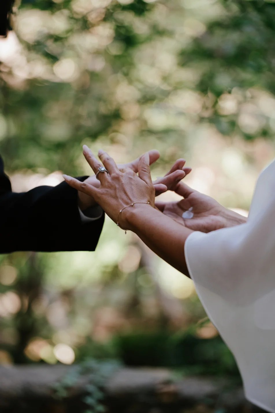 Gros plan sur les mains d'un couple s'unissant, avec bague et bracelet, dans un cadre naturel et lumineux.