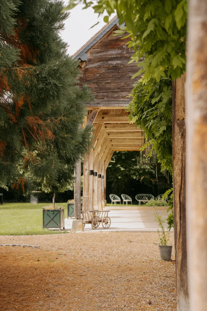 Grange rustique en bois avec terrasse ombragée et jardin verdoyant, ambiance champêtre et lumineuse.