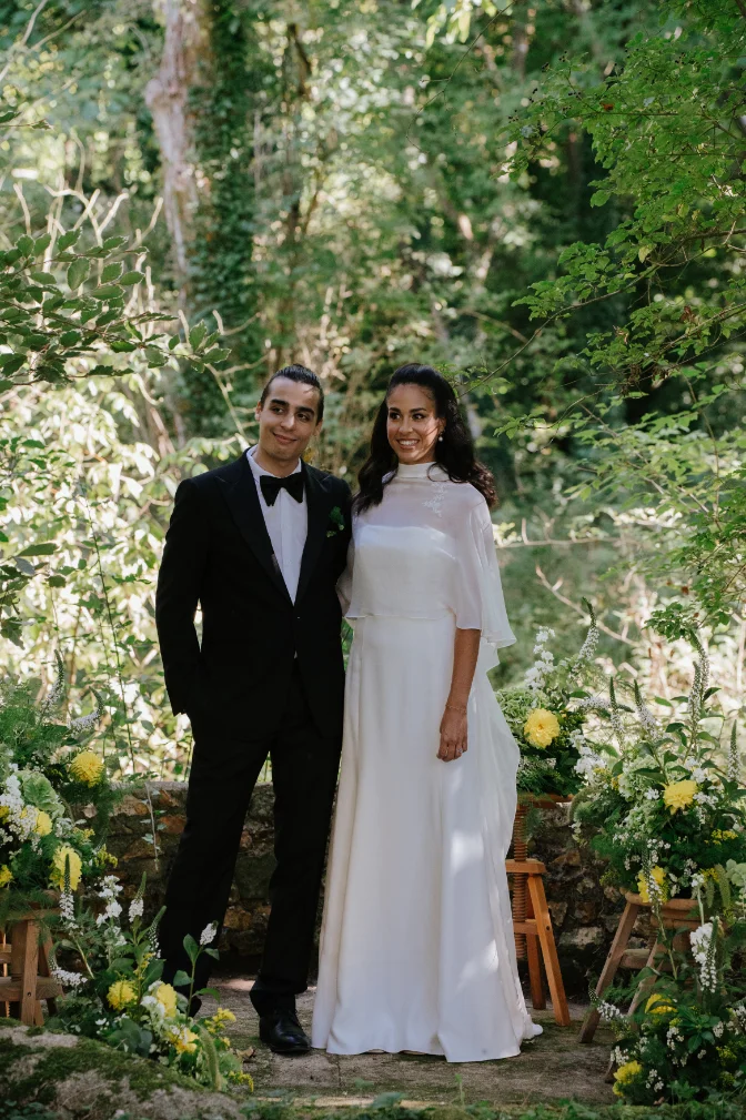 Couple élégant en tenue de mariage posant dans un jardin luxuriant et lumineux.
