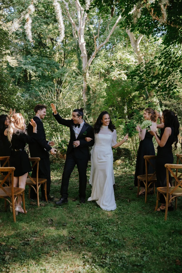 Jeunes mariés rayonnants et leurs invités célébrant avec joie dans un jardin verdoyant et lumineux.