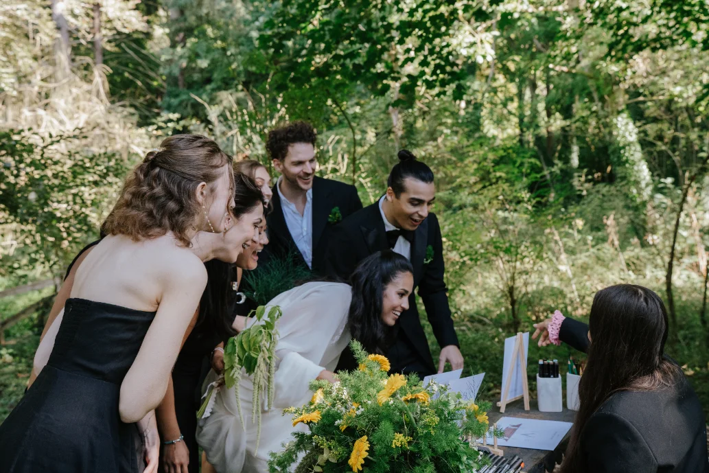 Un groupe d'invités élégants admire avec sourire un portrait peint en plein air dans un jardin verdoyant.
