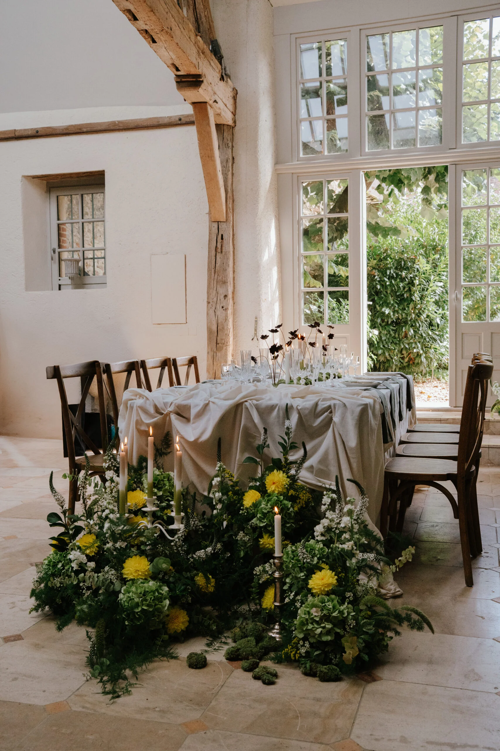 Table de mariage élégante avec nappe crème, fleurs sauvages jaunes et blanches et bougies dans un intérieur rustique.