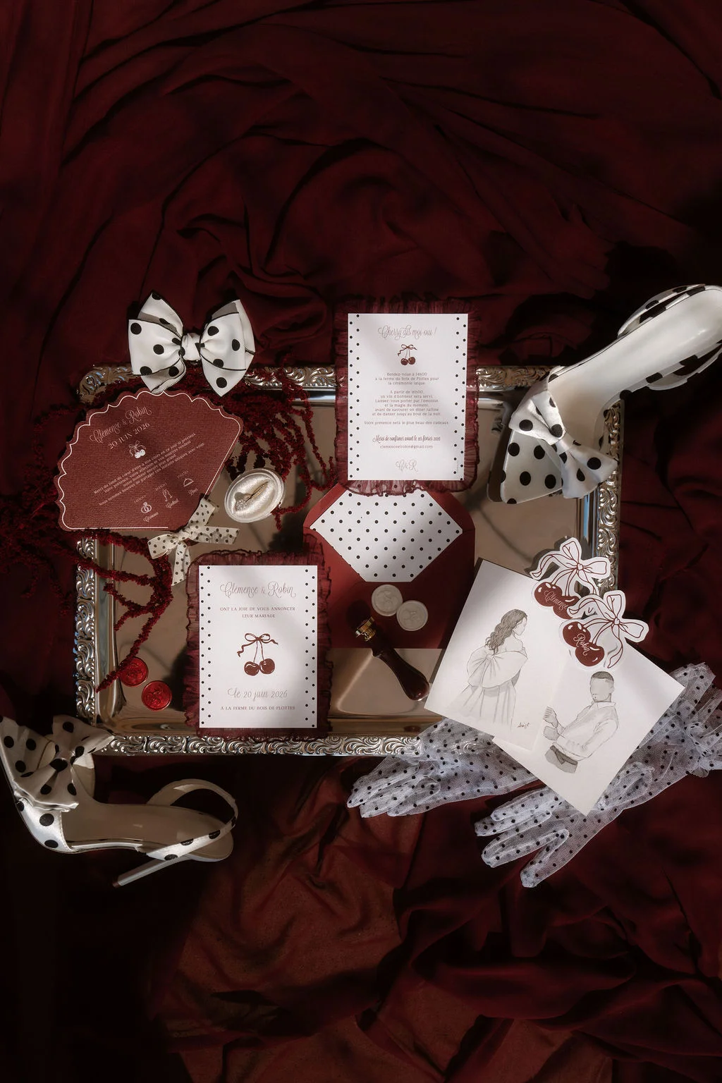 Papeterie de mariage rouge et blanche à pois, avec chaussures et accessoires assortis sur un drapé de satin bordeaux.