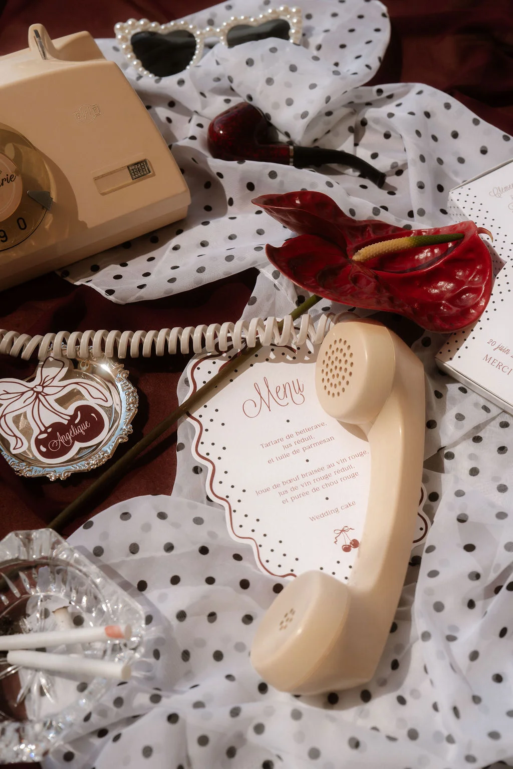 Composition vintage aux tons crème et rouge avec téléphone rétro, menu de mariage et tissu à pois blancs et noirs.