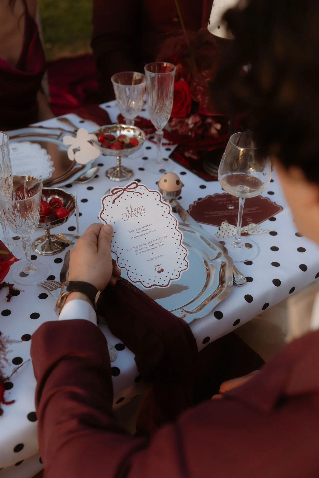 Table dressée aux tons bordeaux et blanc à pois avec menu élégant et coupes de cerises pour un mariage chic.