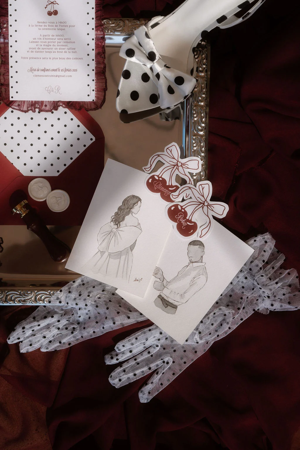 Papeterie de mariage et accessoires à pois sur fond rouge bordeaux, avec illustrations minimalistes et gants de dentelle.
