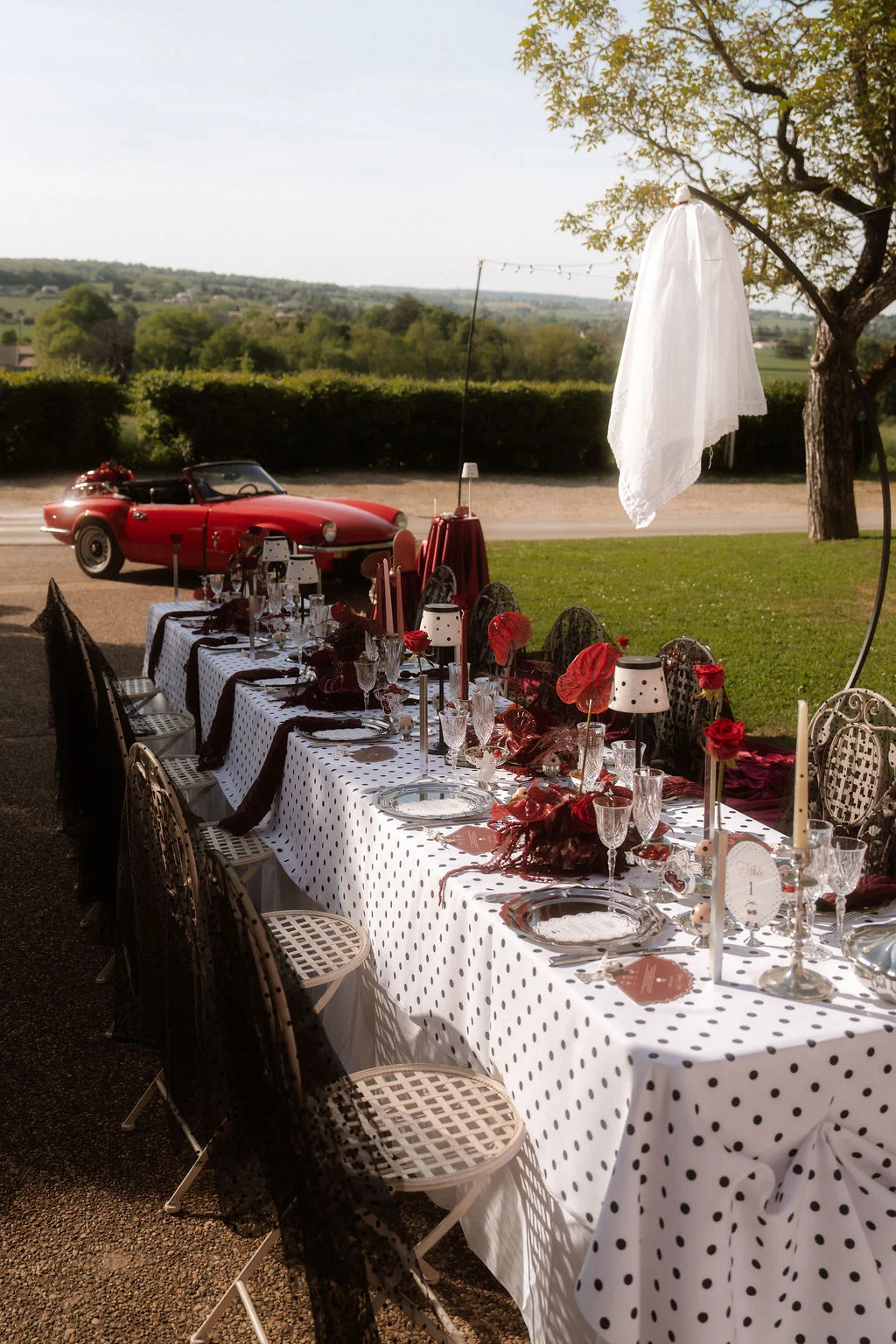 Table de mariage élégante à pois blancs et noirs, décorée de roses rouges, avec une voiture ancienne rouge en arrière-plan.