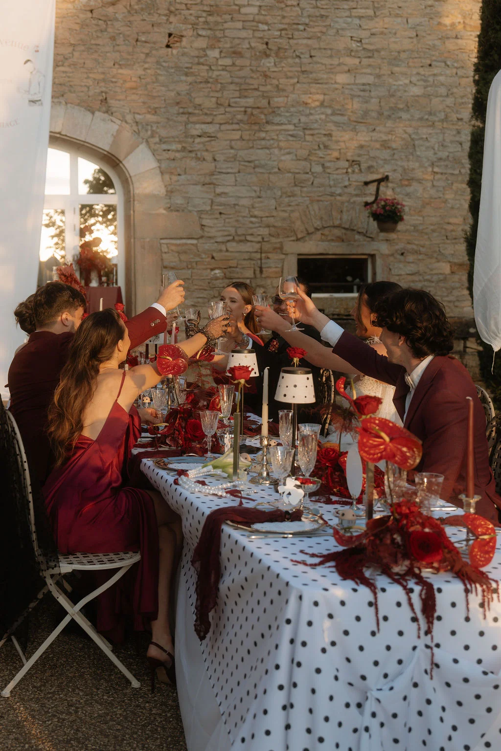 Dîner élégant aux tons cerise et blanc à pois, avec des invités trinquant autour d'une table richement décorée.