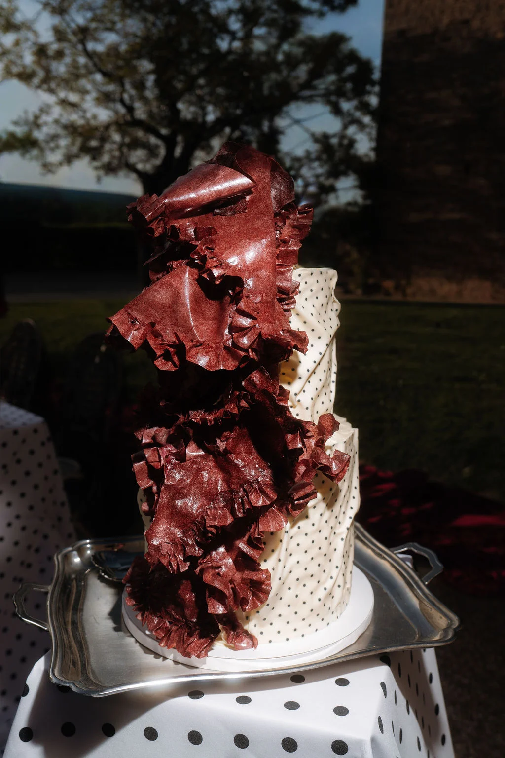 Gâteau blanc à pois noirs orné de volants en chocolat rouge cerise, posé sur un plateau argenté.