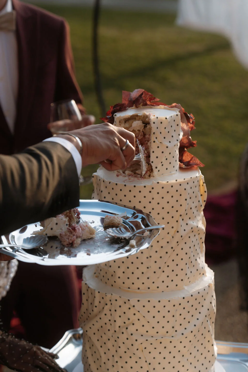 Une main coupe une part de gâteau de mariage à pois blancs et noirs, décoré de fleurs rouges.