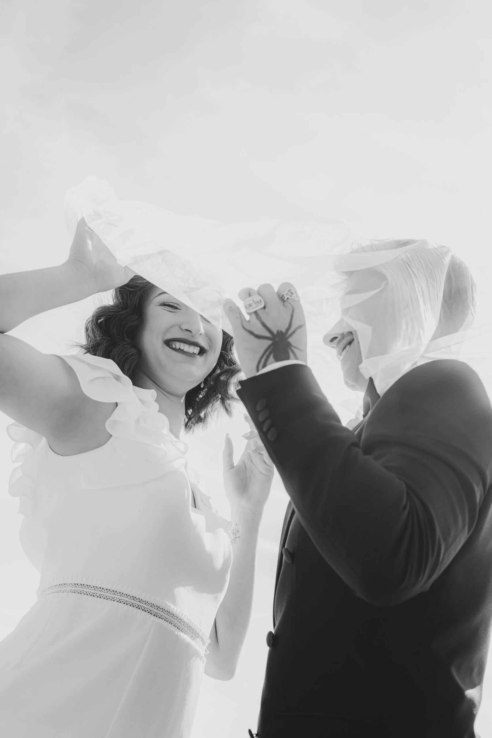 Couple riant sous un voile blanc dans une ambiance rétro, photographie en noir et blanc.