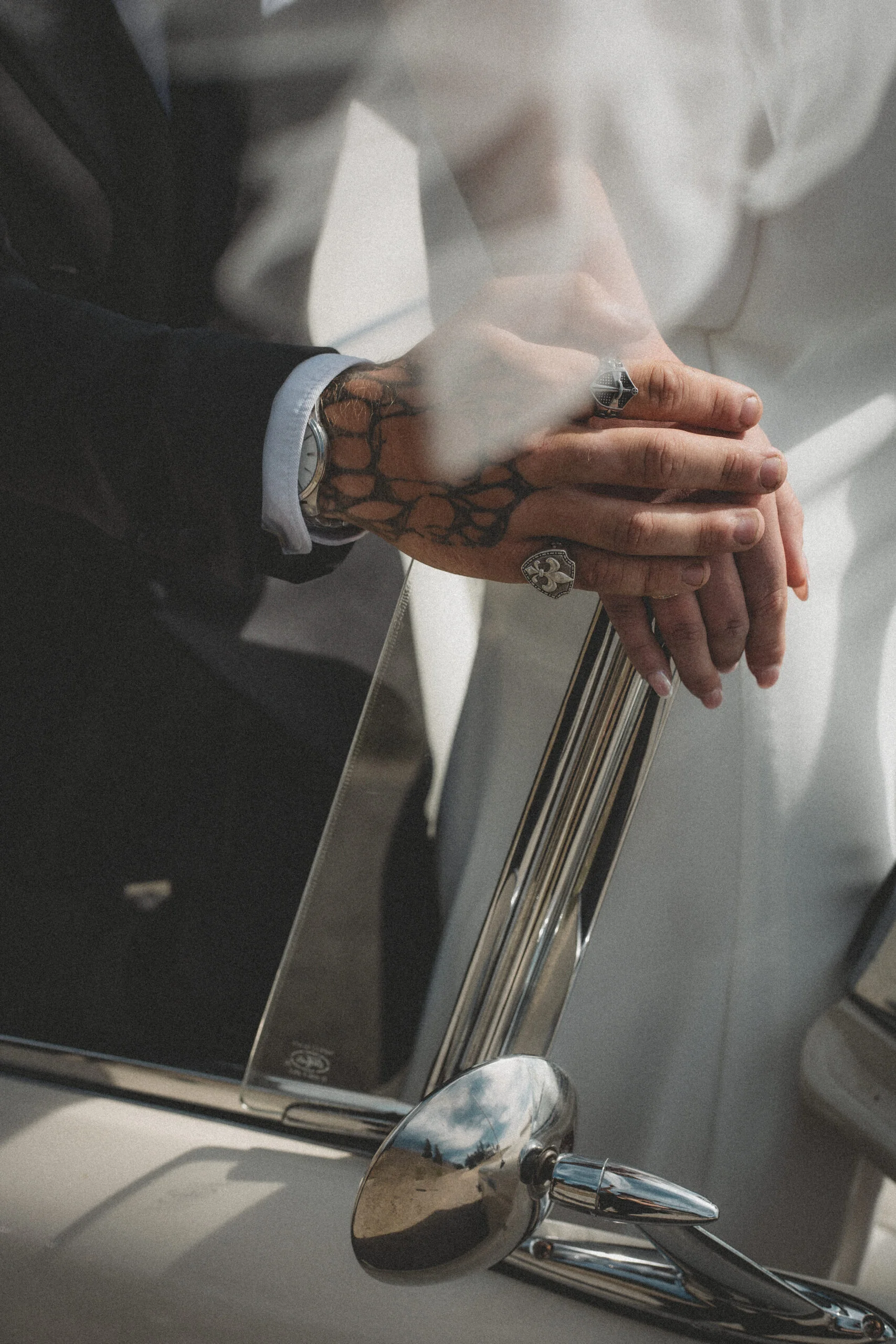 Gros plan romantique des mains d'un couple tatoué sur le chrome d'une voiture ancienne, ambiance rétro et élégante.