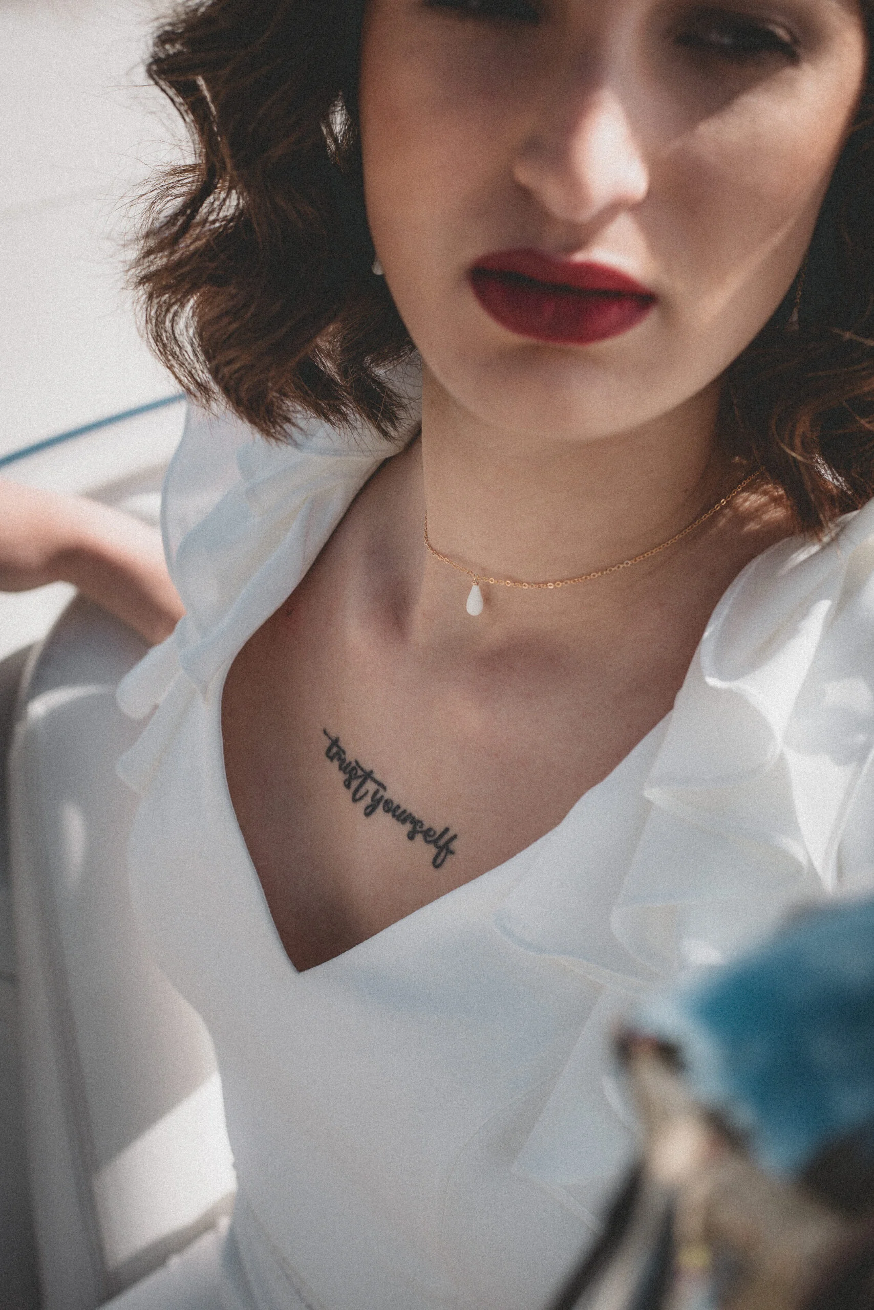 Gros plan d'une mariée au look rétro avec rouge à lèvres sombre et tatouage "trust yourself" sur le décolleté.