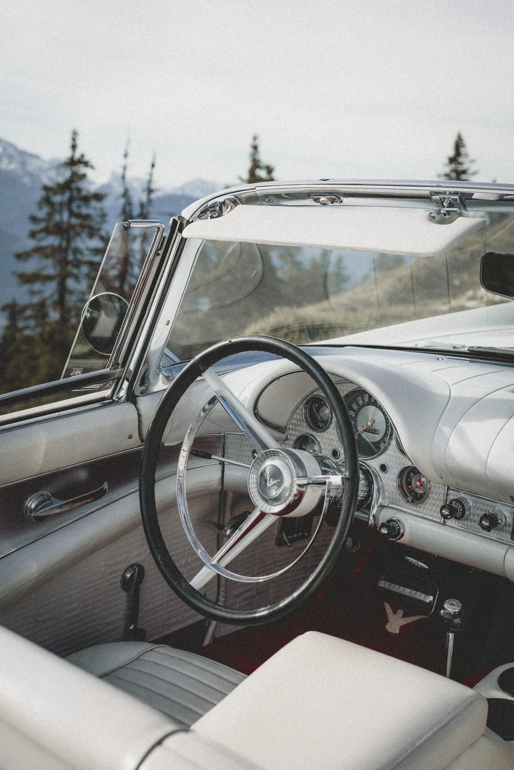 Intérieur blanc et chrome d'une voiture de collection décapotable dans un paysage montagneux et romantique.