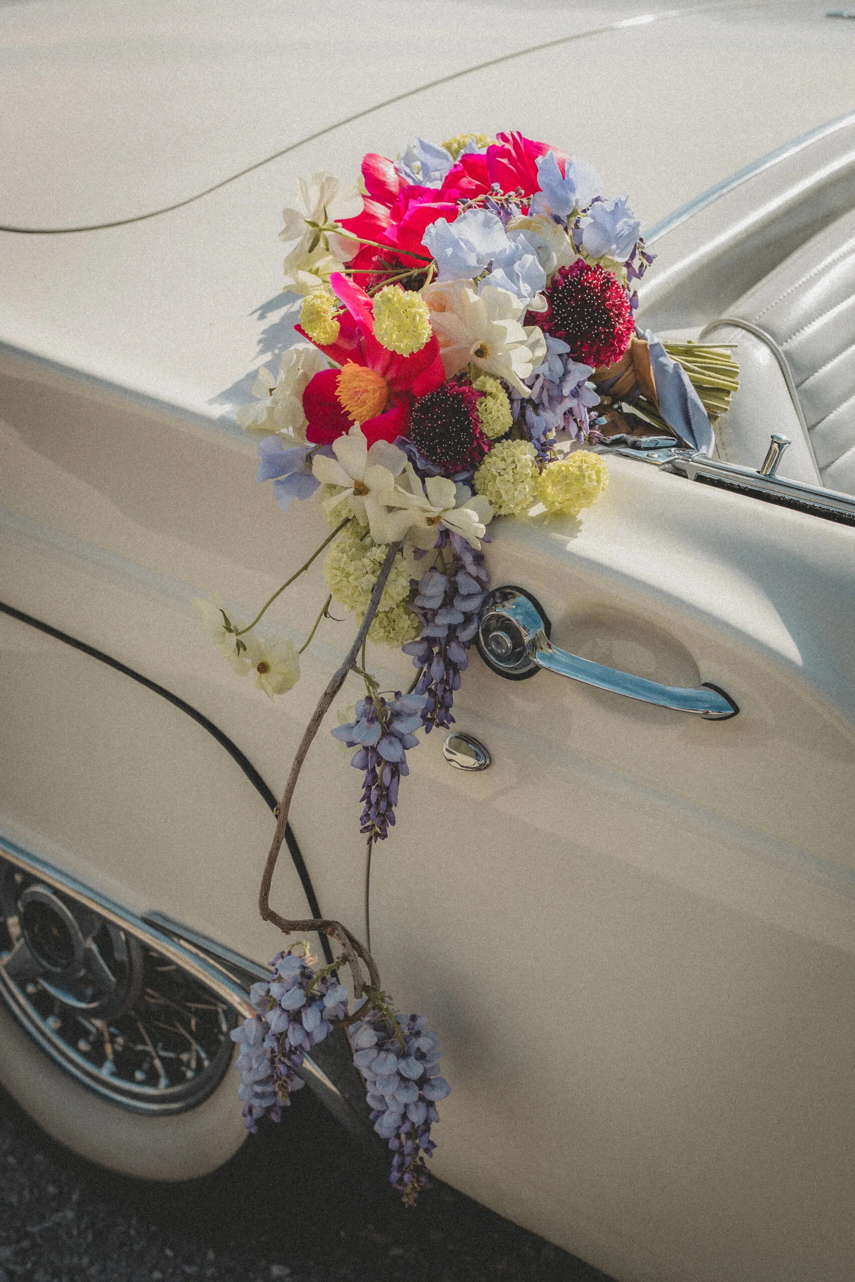 Bouquet de fleurs colorées posé sur la portière d'une voiture ancienne crème pour une ambiance rétro romantique.