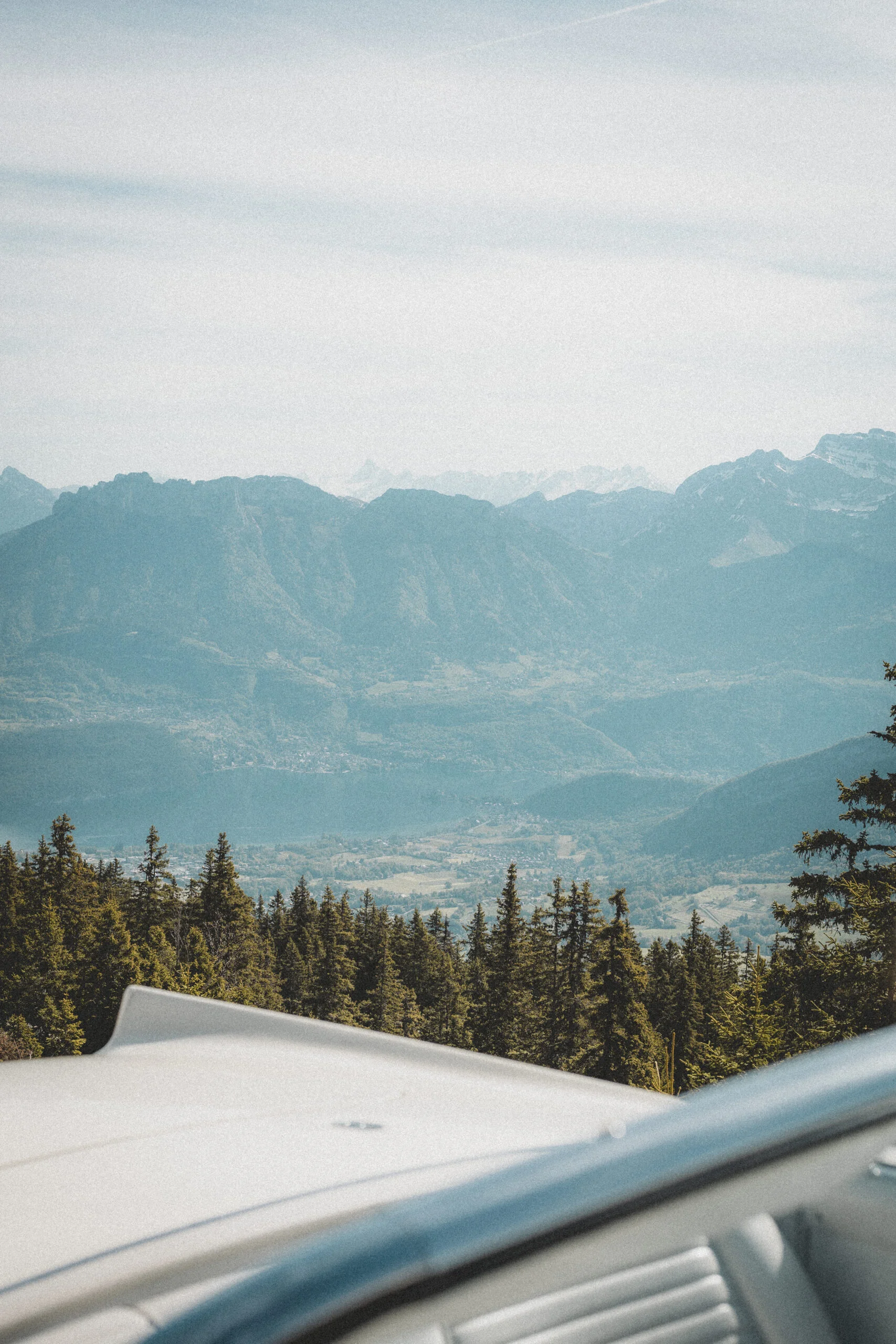 Vue panoramique sur des montagnes bleutées depuis le capot d'une voiture blanche vintage, ambiance douce et nostalgique.