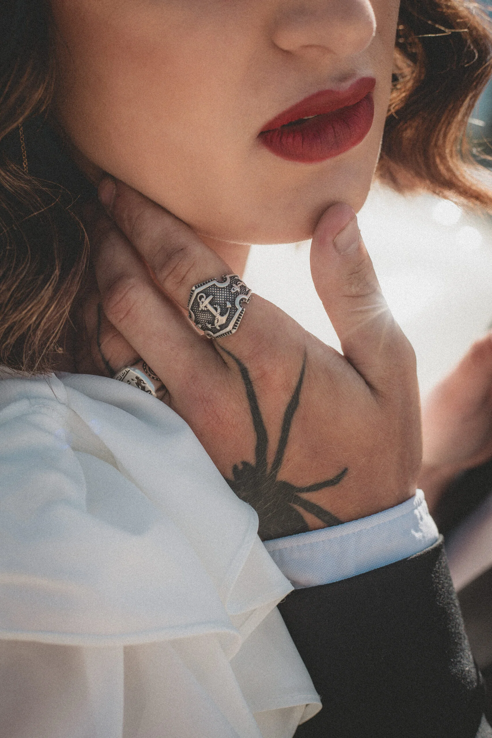 Gros plan rétro d'une femme aux lèvres rouges, portant une bague anchor et des tatouages, dans une ambiance romantique.