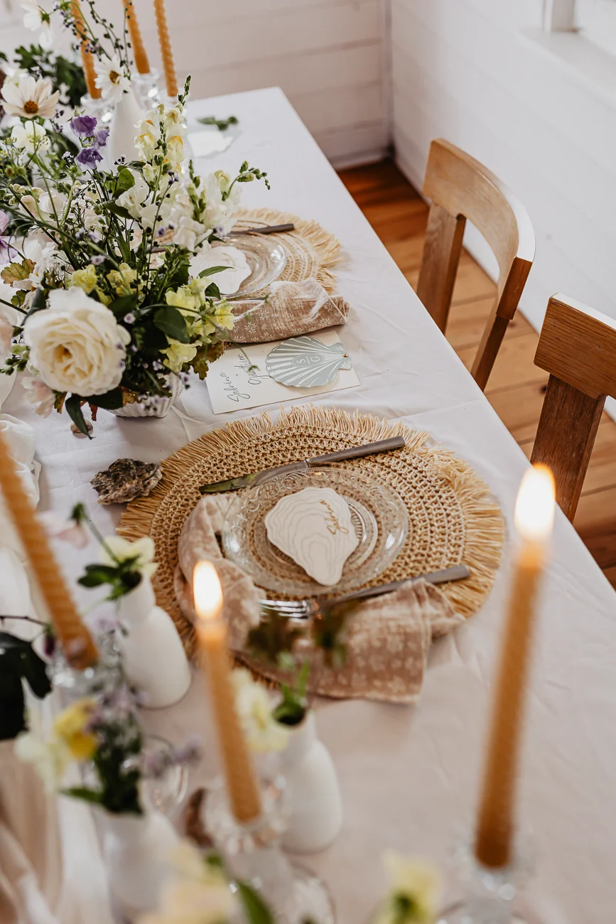 Table dressée dans des tons crème et naturels avec fleurs blanches, bougies et détails nacrés pour un mariage bohème.