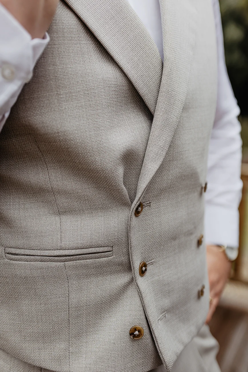 Gros plan sur un gilet de costume beige texturé porté sur une chemise blanche pour un look de mariage élégant.