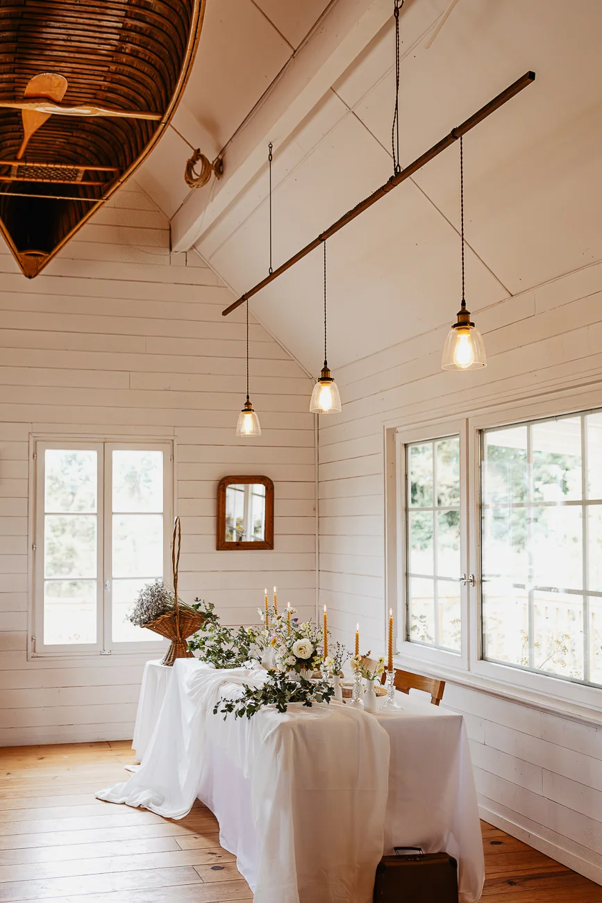 Table de mariage élégante avec fleurs blanches et bougies dans une pièce lumineuse aux murs blancs et style rustique.