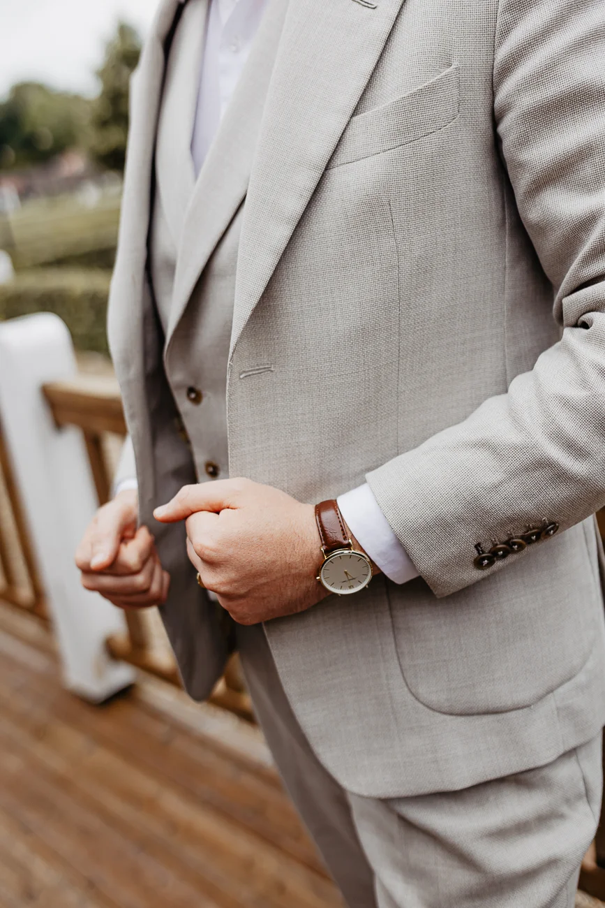 Gros plan d'un marié élégant en costume trois-pièces beige clair avec une montre en cuir marron.