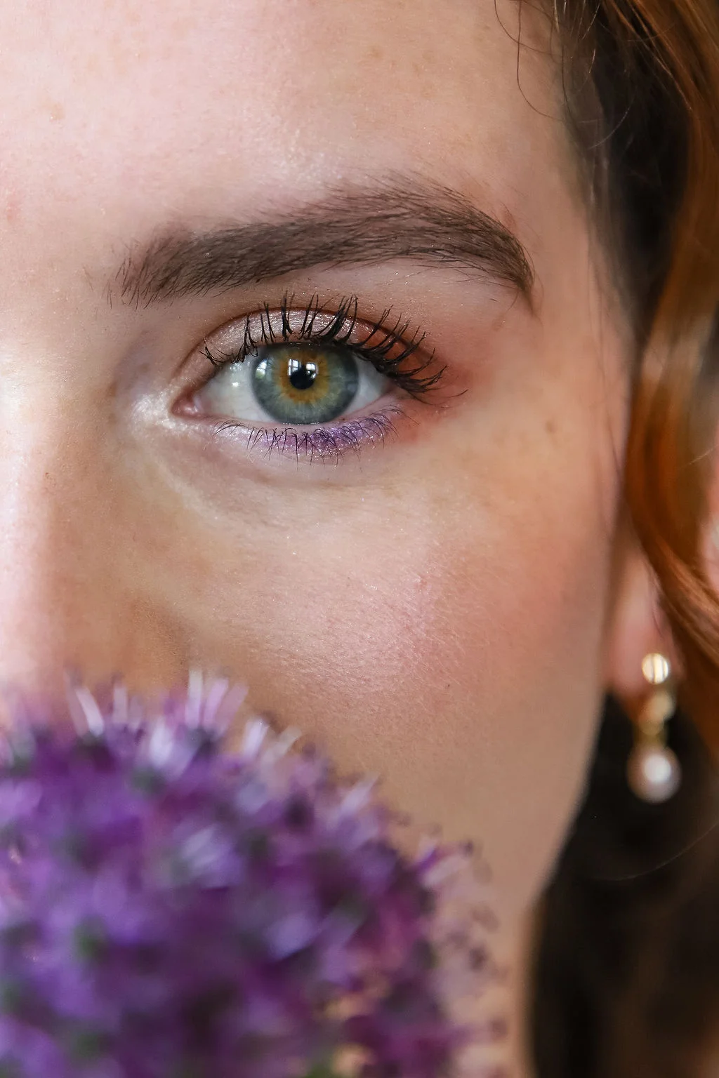 Gros plan romantique sur le regard d'une femme aux yeux clairs, partiellement masqué par des fleurs violettes.