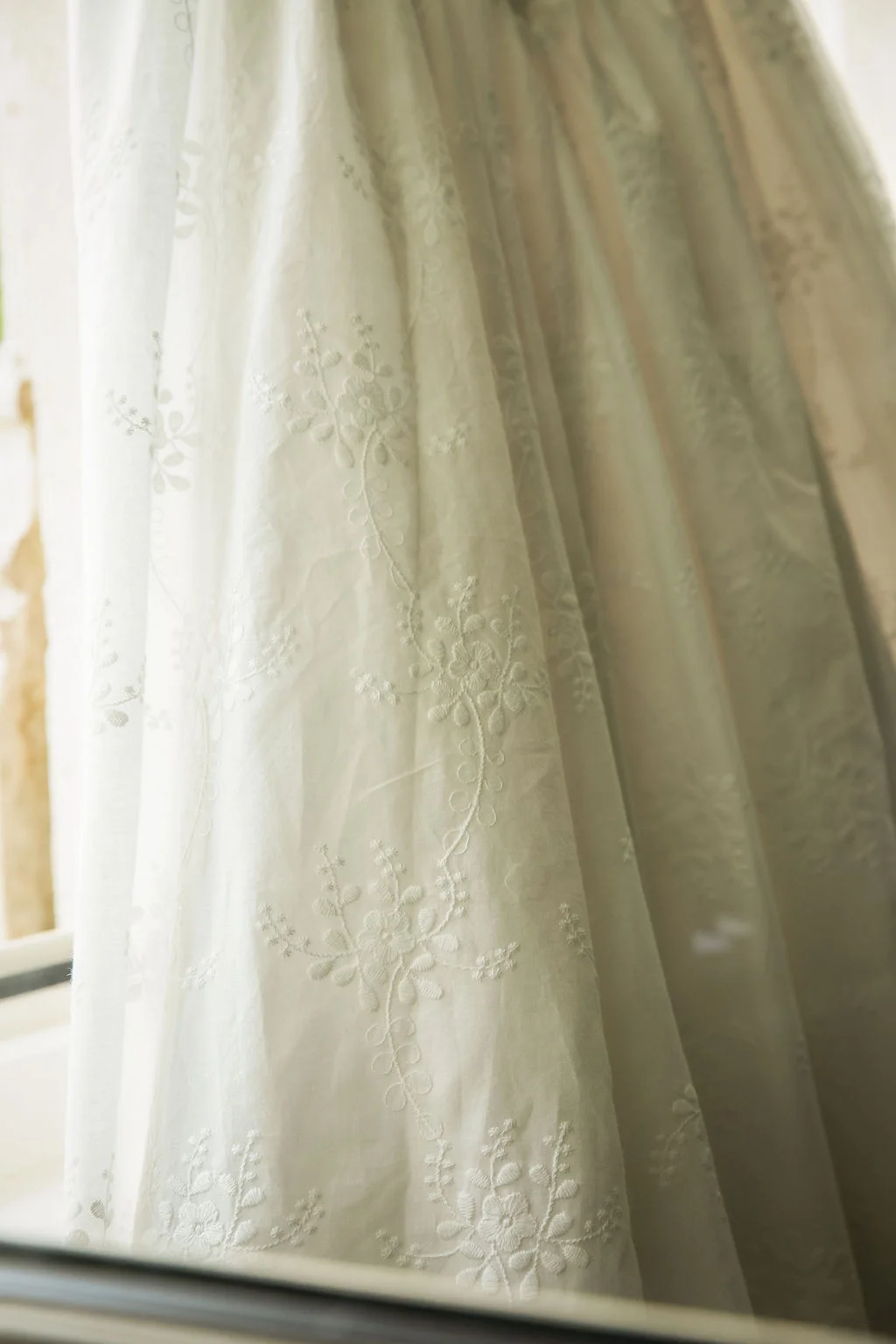 Détail romantique d'un tissu blanc brodé de fleurs, drapé avec légèreté dans une ambiance lumineuse et douce.