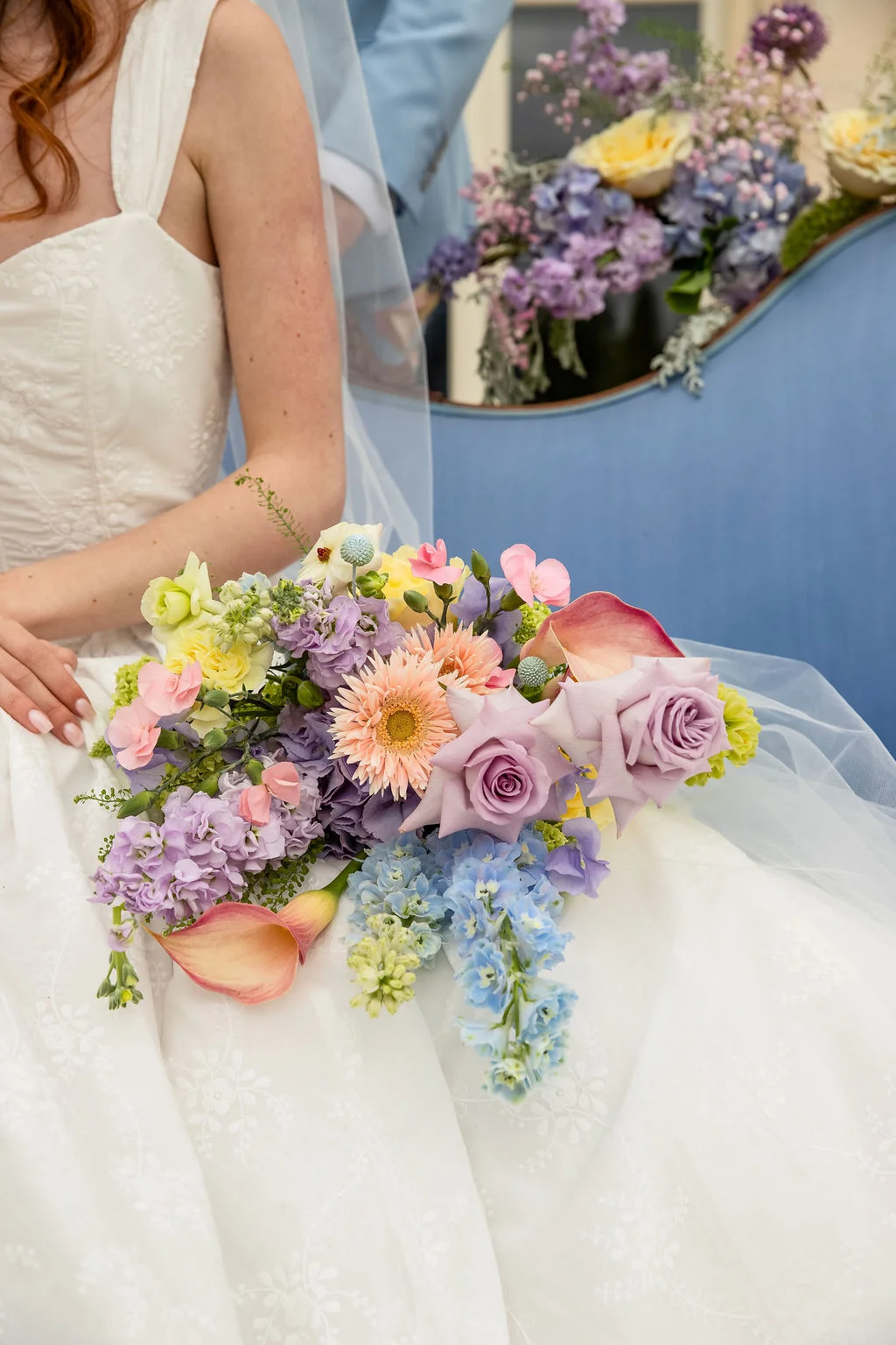 Mariée en robe blanche tenant un bouquet romantique aux nuances pastel de rose, mauve, bleu et jaune.