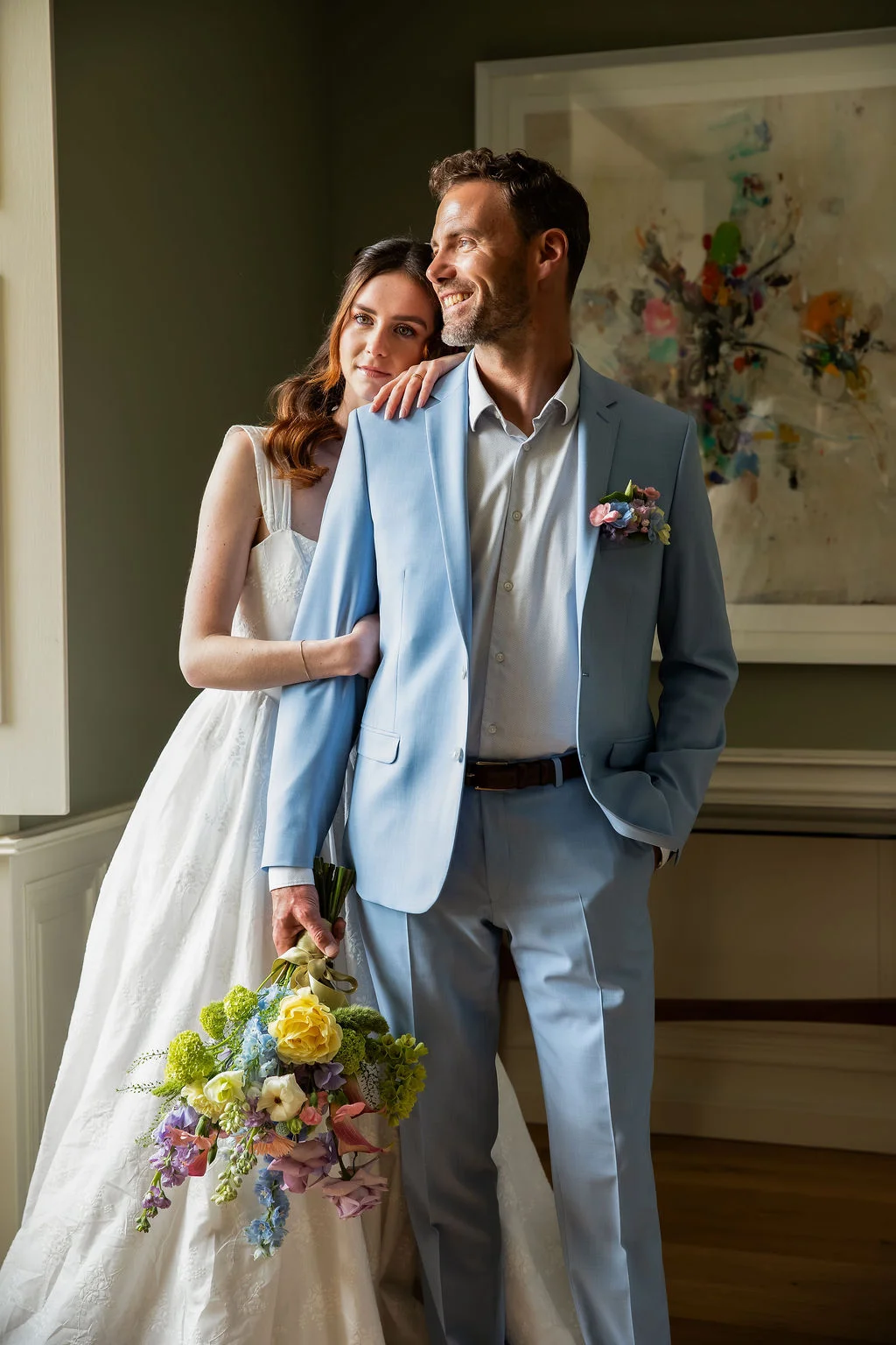 Couple de mariés complices, elle en robe blanche et lui en costume bleu ciel, avec un bouquet coloré.