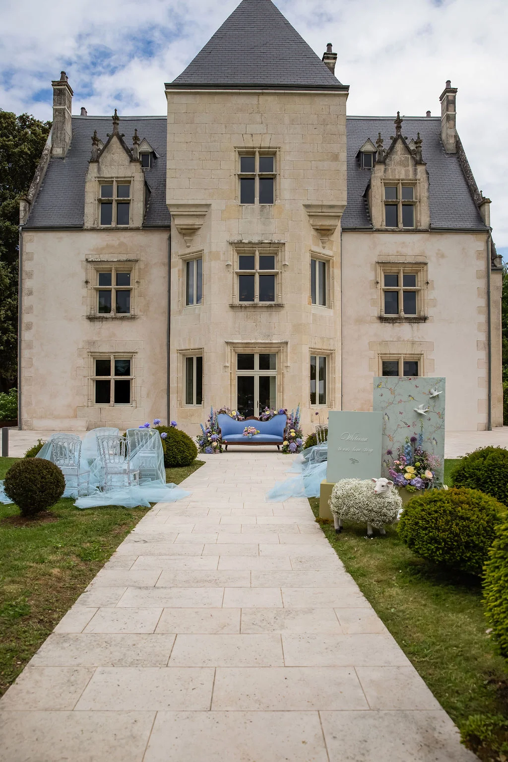 Décoration romantique bleu pastel avec canapé et fleurs devant un château en pierre claire.