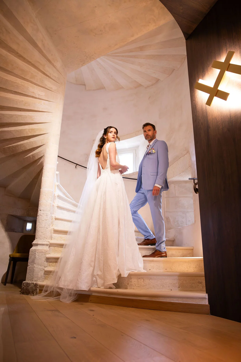 Couple marié élégant posant sur un escalier en pierre blanche dans un intérieur romantique et lumineux.