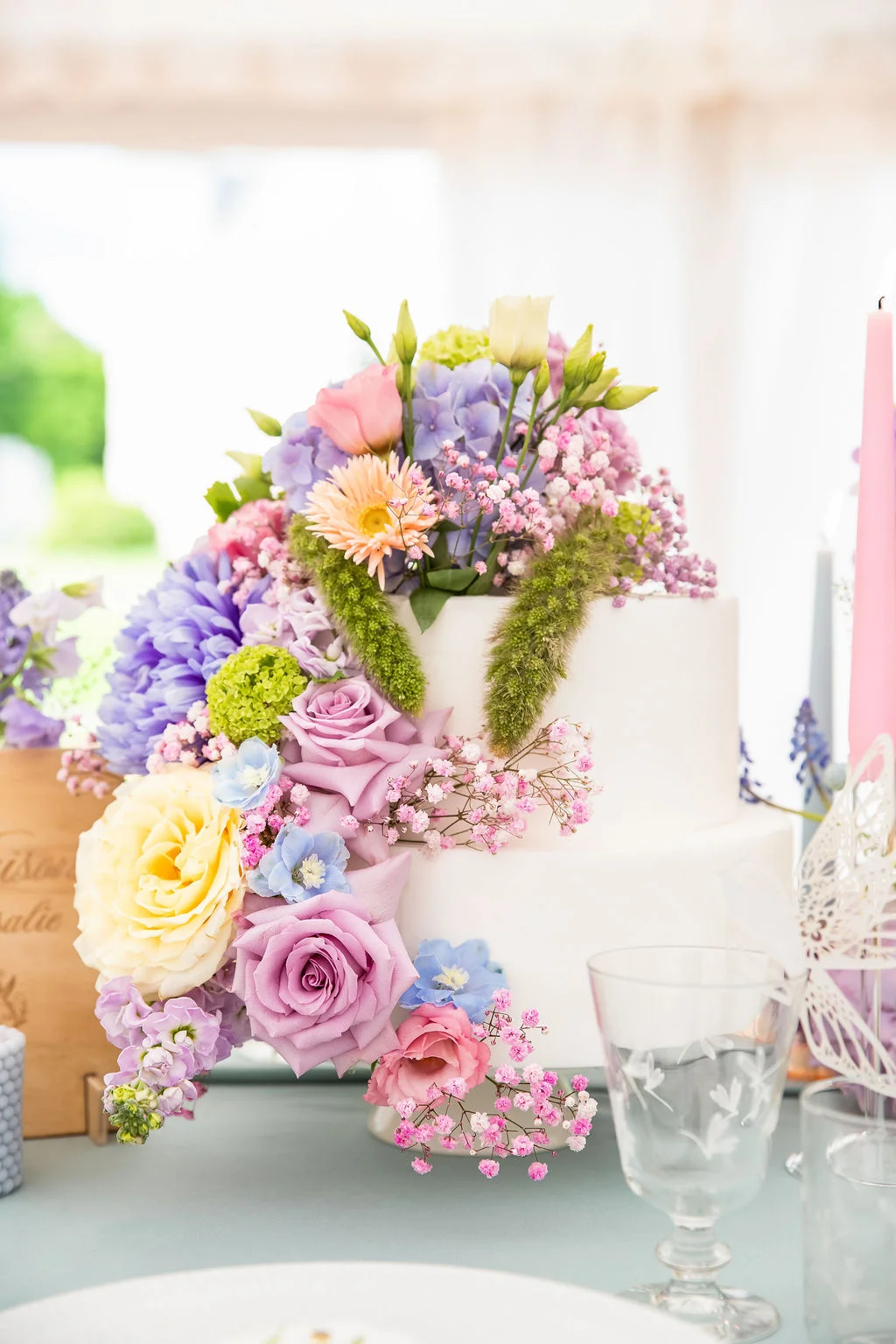 Gâteau de mariage blanc à deux étages, décoré d'une cascade de fleurs romantiques aux tons pastel, rose, mauve et jaune.