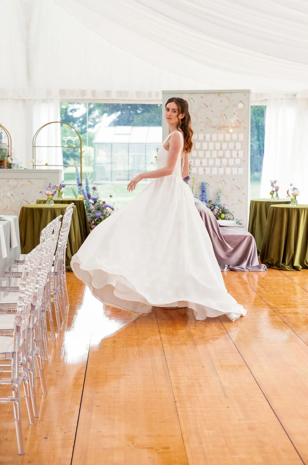 Une mariée en robe blanche vaporeuse pose avec élégance dans un chapiteau lumineux et romantique.