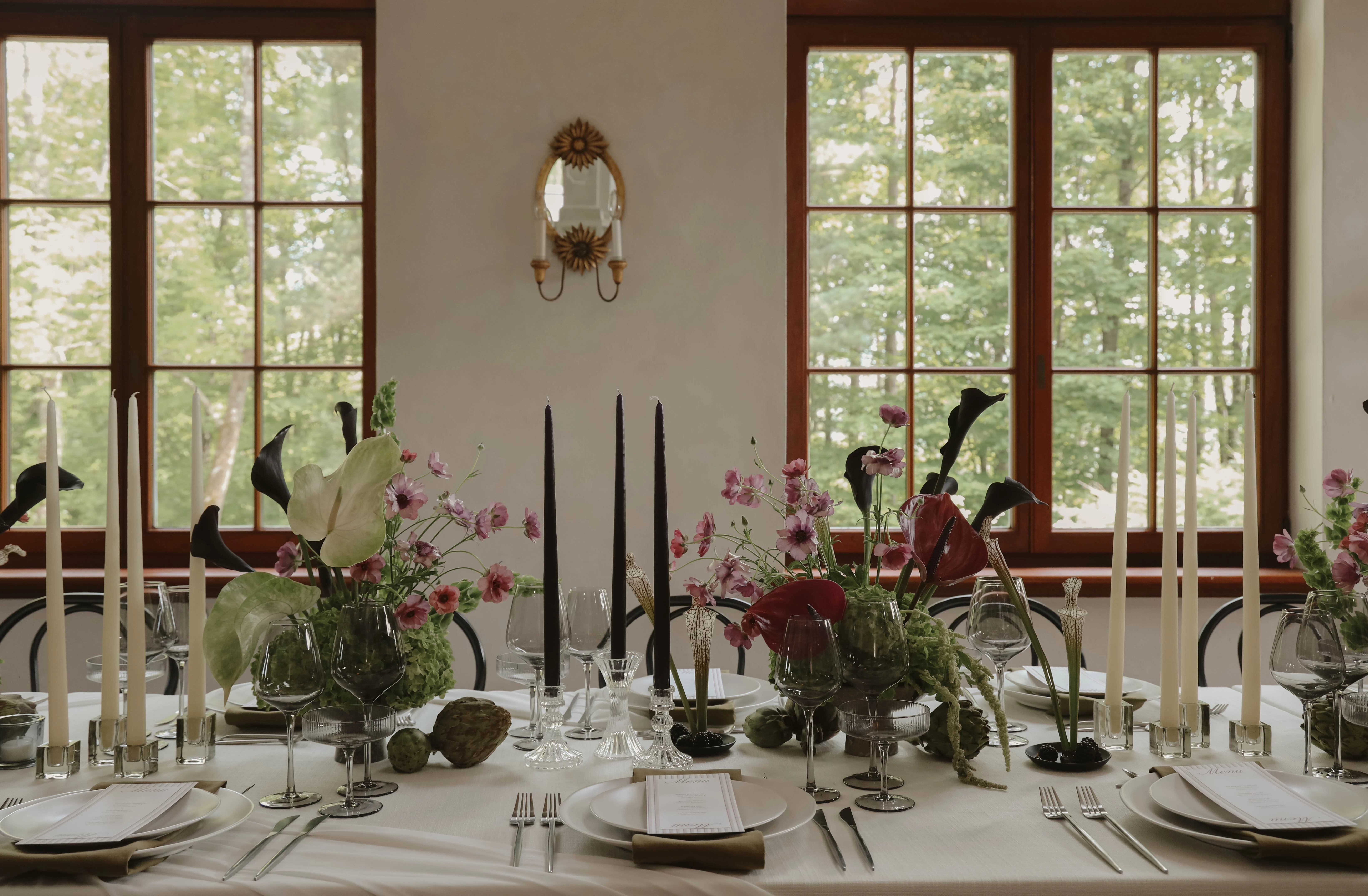 Table de mariage minimaliste avec compositions florales pastel, bougies fines et art de la table épuré devant des fenêtres.