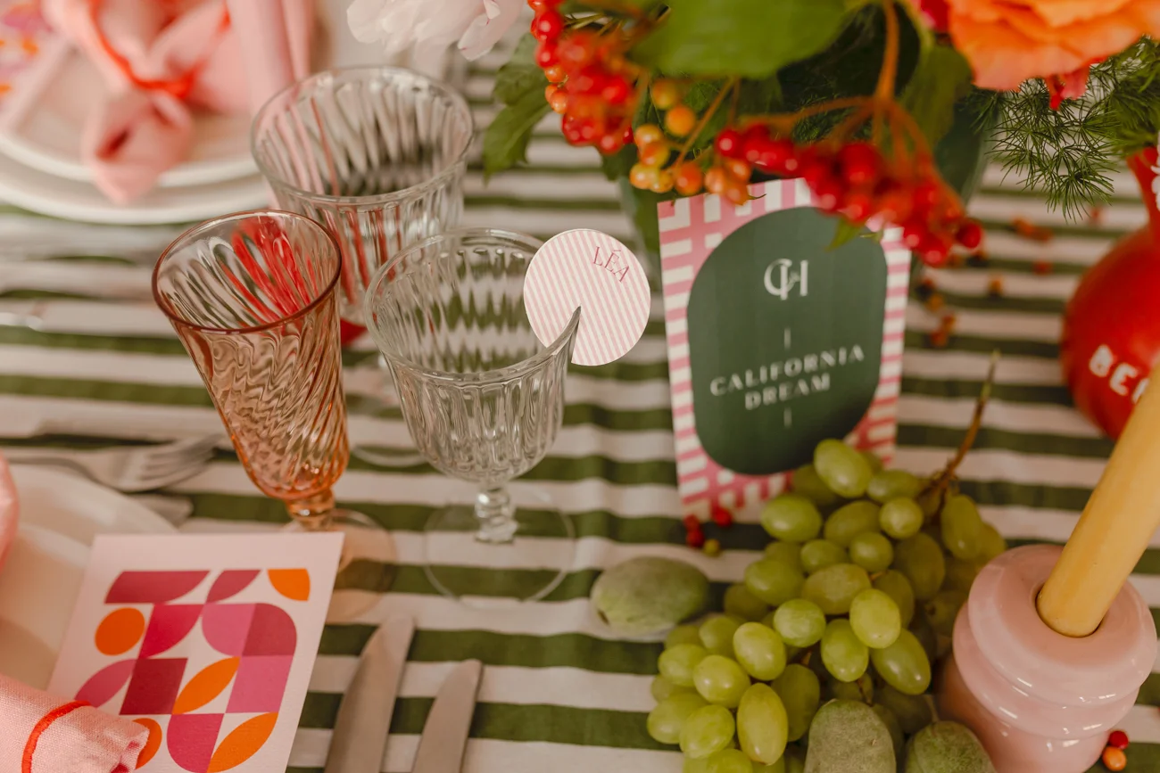 Table dressée rétro avec nappage rayé vert, verres ciselés, raisins et touches de rose et rouge.
